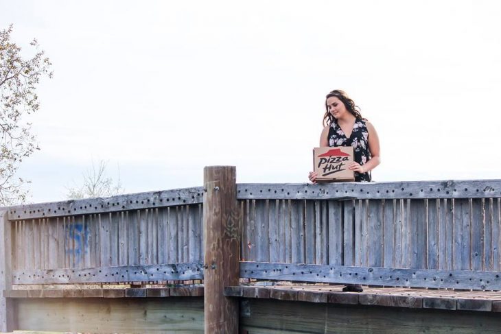 Chica paseando por un puente mientras carga una caja de pizza