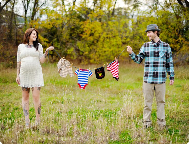 Sesión de fotos de maternidad pareja sosteniendo la ropa del bebé