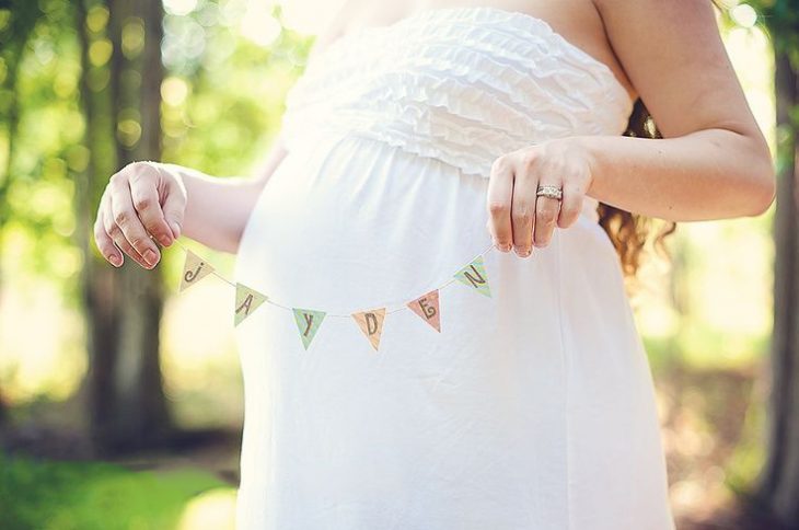 Sesión de fotos de maternidad chica sosteniendo el nombre de su bebé junto a su vientre 