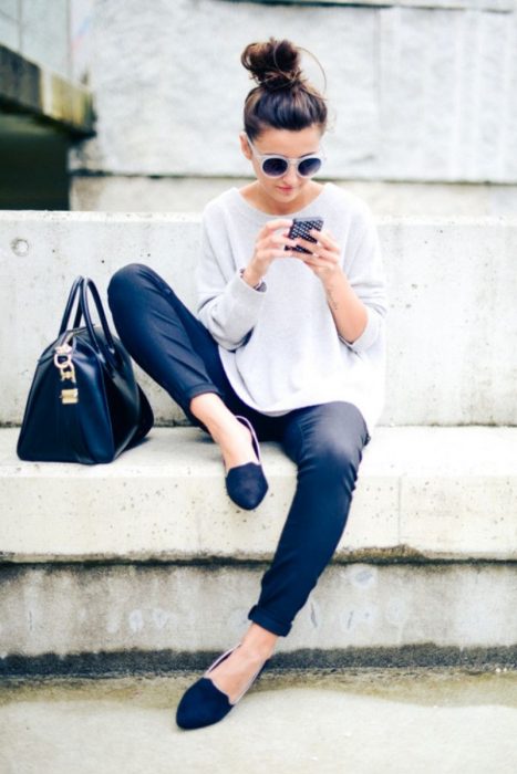 Chica sentada en una banca de la calle viendo su celular 