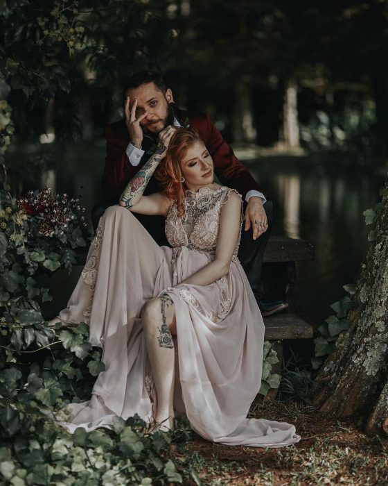 Sesión de fotos de recién casados en boda vikinga, esposos sentados en la naturaleza entre árboles