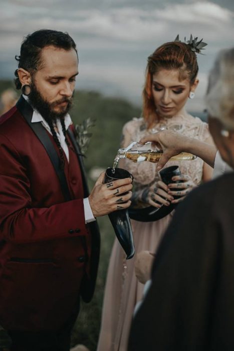 Pareja de novios celebra una boda nórdica al aire libre, novios con tatuajes y expansiones, beben hidromiel en cuernos vikingos