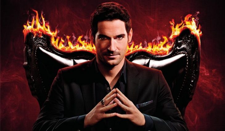 Hombre con traje sastre negro cruzando las manos sentado en una silla con llamas, escena de la serie Lucifer