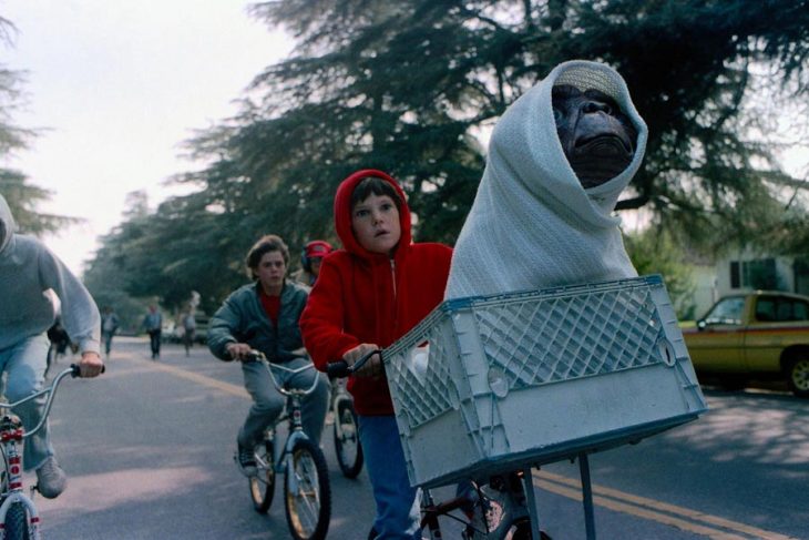 Niños paseando en bicicleta llevando un muñeco de pelucho de un extraterrestre en una cesta, escena de la película E.T., el extraterrestre 