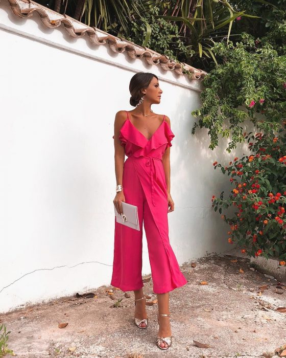 Chica usando un jumpsuit de color rosa con zapatos y accesorios plateados mientras posa para una foto durante una sesiÃ³n en un jardÃ­n 