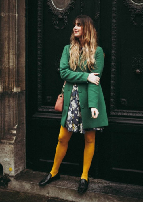 Outfits con medias de colores; chica posando frente a puerta,, con medias amarillas, vestido de flores y saco verde