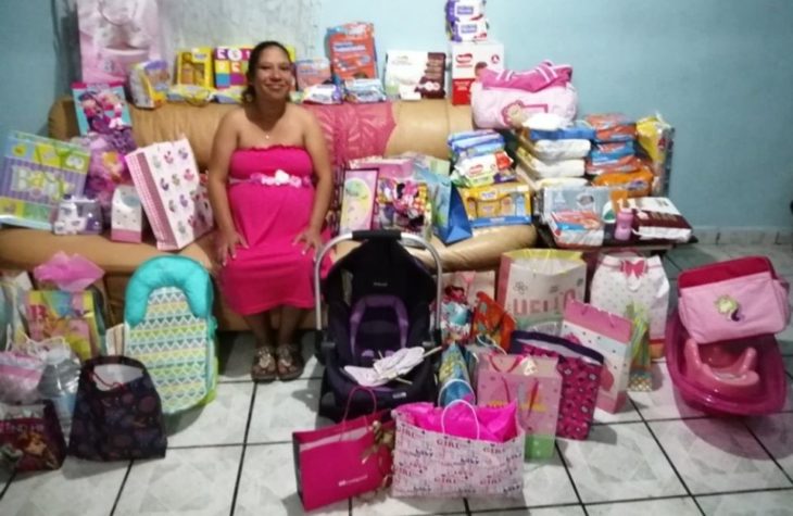 Mujer sentada en un sofá rodeada de regalos para su futura bebé