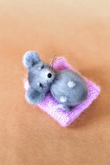 Peluche creado por la artista Svetlana Gromova, ratón miniatura de color gris recostado en una sábana rosa