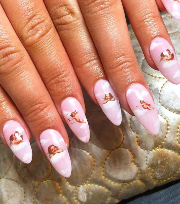 Manicura con diseño de cielo y nubes; uñas largas en forma de almendra pintadas con esmalte rosa bebé y ángeles querubines