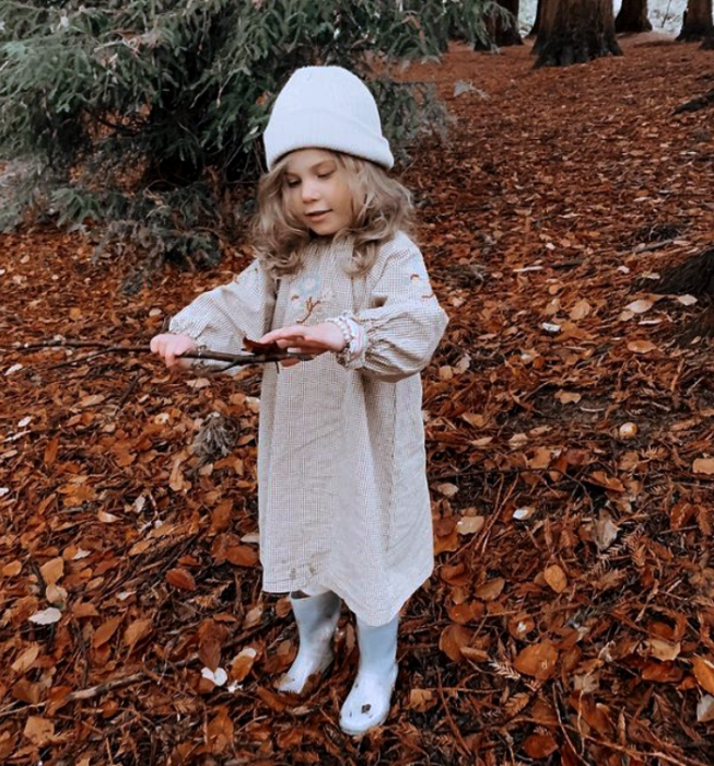 niña rubia usando un sombrero blanco tejido, vestido largo beige de manga larga, botas blancas